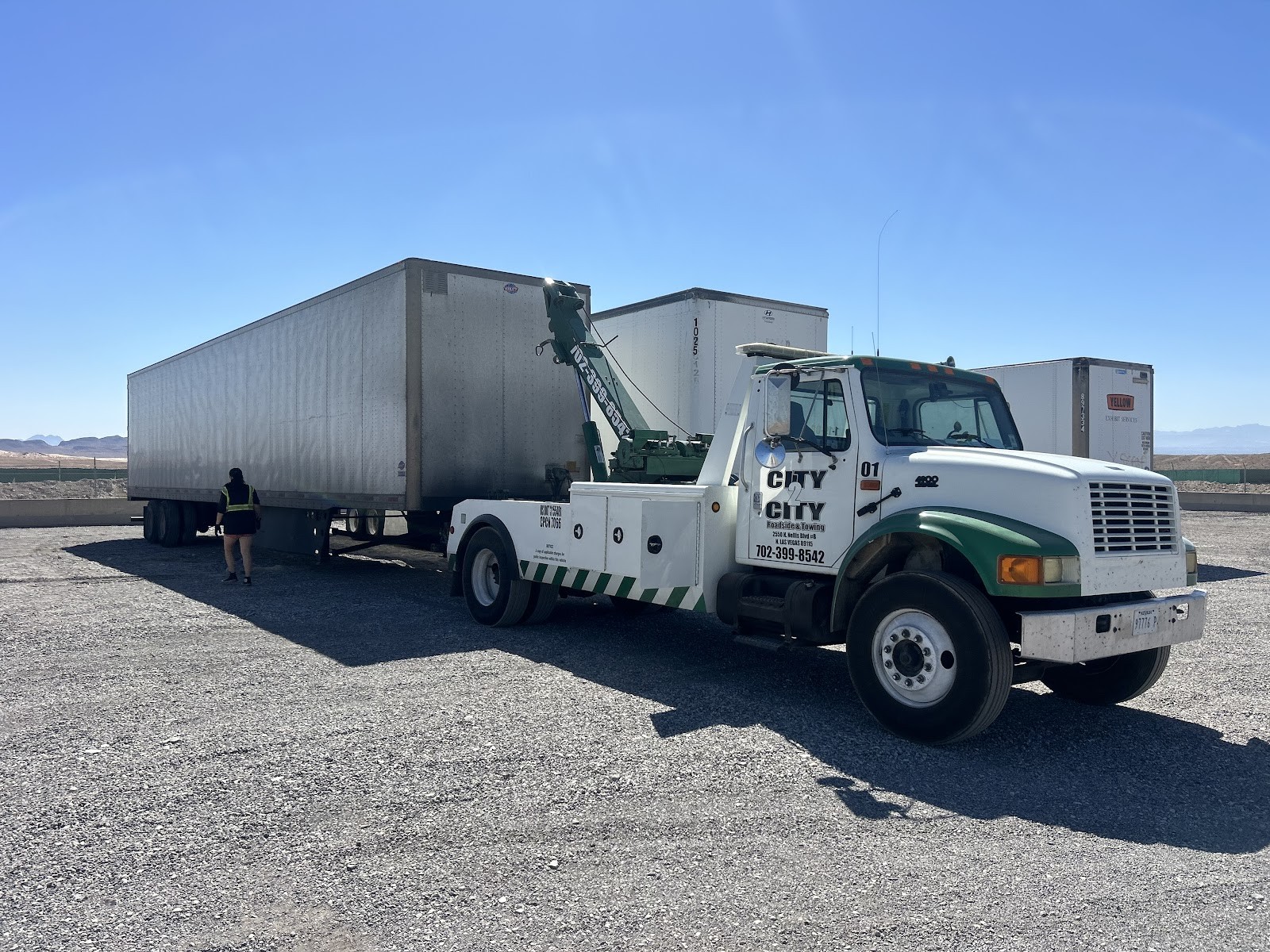 City 2 City wrecker hooked to a semi-trailer in an open lot with a worker