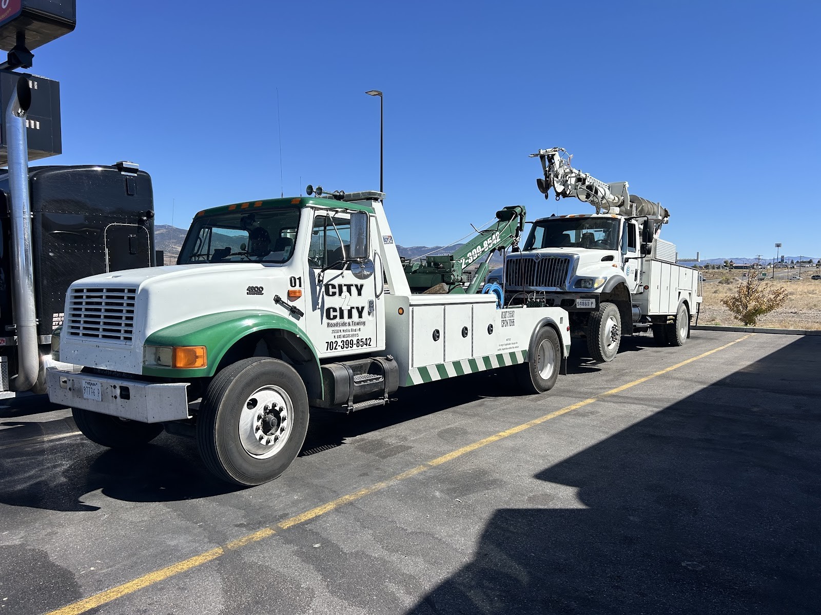 City 2 City wrecker towing a utility digger-derrick truck at a fuel stop