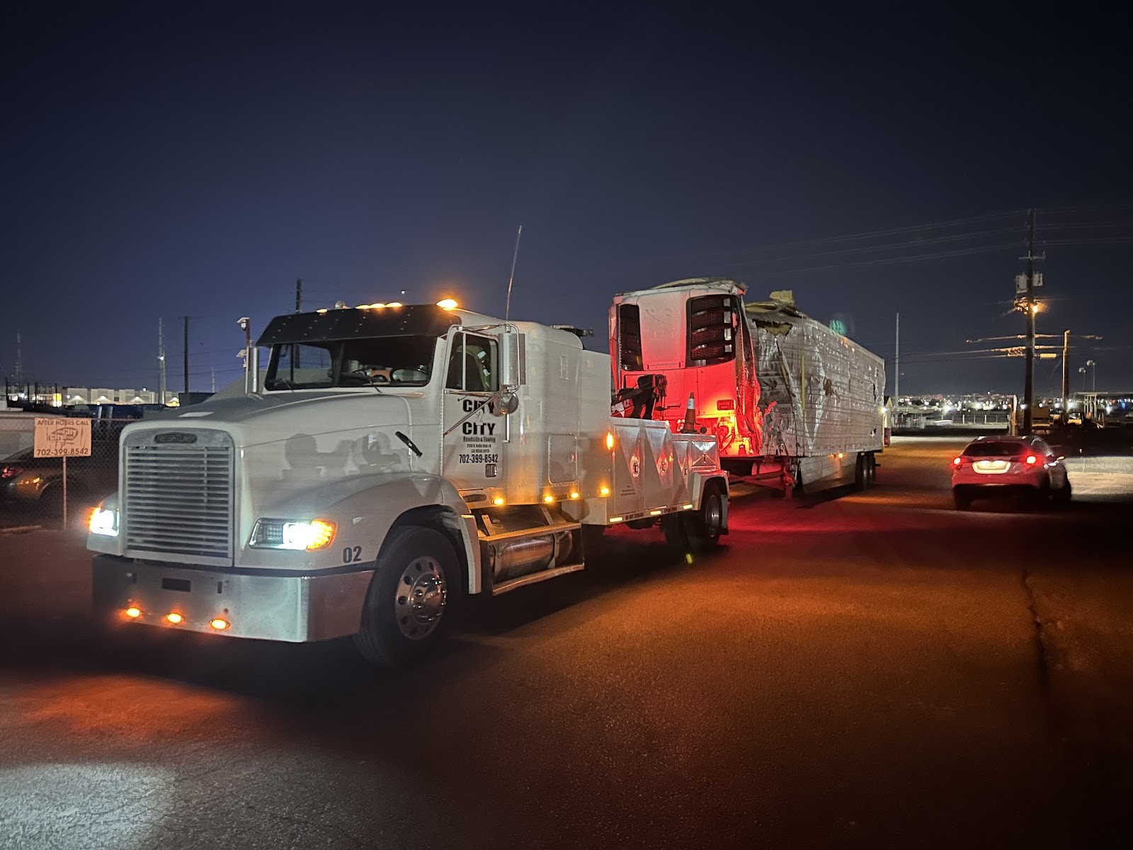 City 2 City tow truck at night with emergency lights towing a large vehicle
